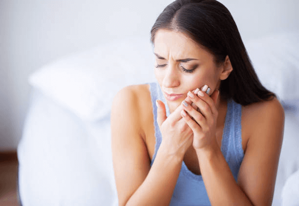 Woman holding her jaw and frowning due to tooth pain.