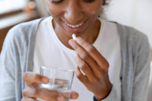 A woman opens her mouth while holding a pill and a glass of water.